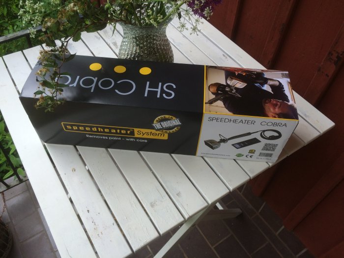 En Speedheater Cobra förpackning på ett vitt bord vid sidan av en vas med vissnade blommor.