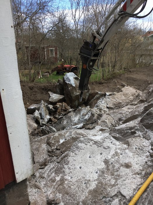 Grävmaskin som utför spräckningsarbete på sten och klippa, stora stenblock syns.