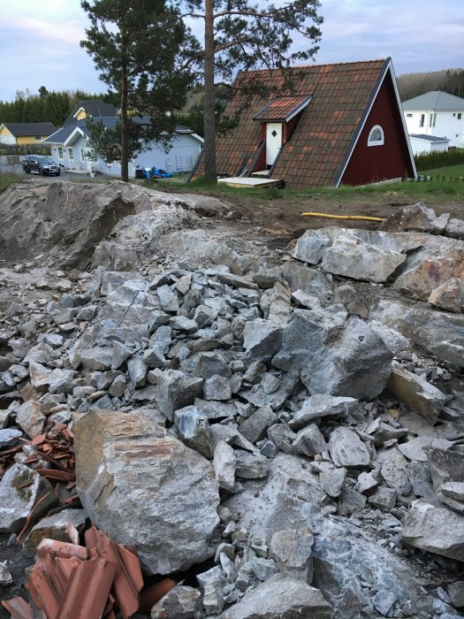 Markarbeten med sten och grus framför rödmålat hus och grönskande träd.