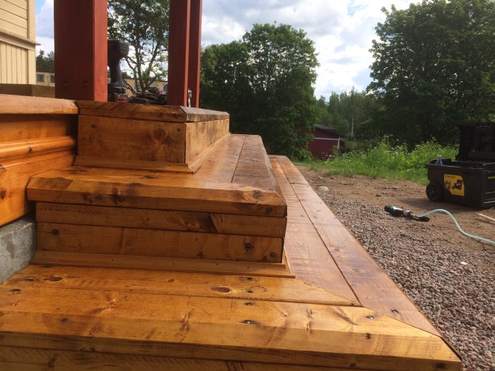 Nybyggd verandatrapp i trä, nymålad i brun ton med roslagsmahogny, vid ett hus.