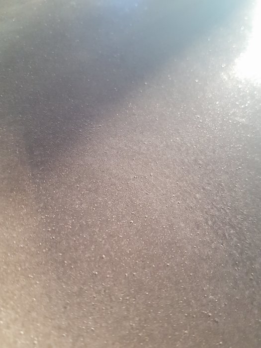 Närbild på en grå yta med dammpartiklar och lätt reflektion av ljus.