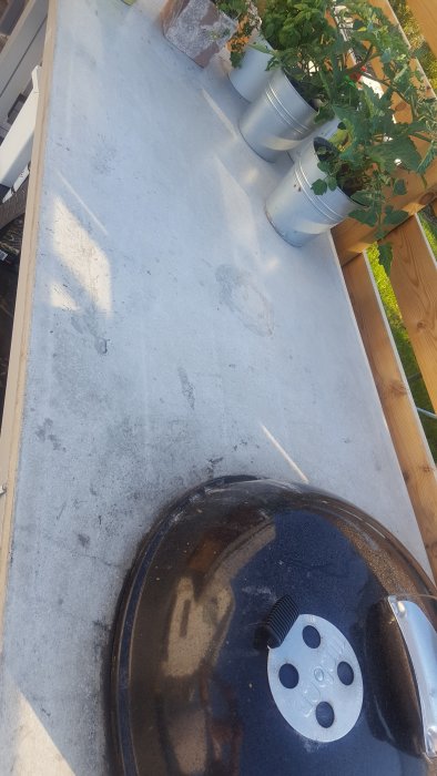 Betonbänkskiva utomhus med fettfläckar och krukväxter, intill grilllock.