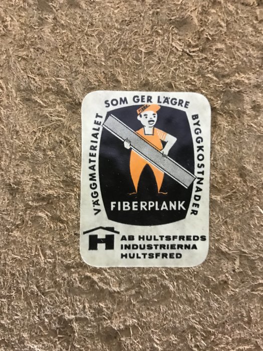 En gammal reklametikett för fiberplank från AB Hultsfreds Industrier på en fibervägg.