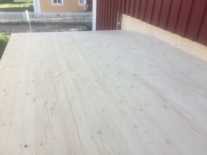 Nyinstallerat trägolv på veranda med plywood-sarg längs husvägg för ventilation.