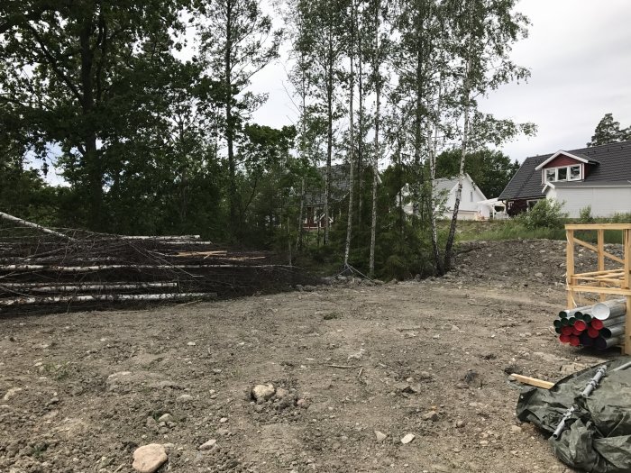 En byggplats med grus och avverkade träd, i bakgrunden syns hus och träd.