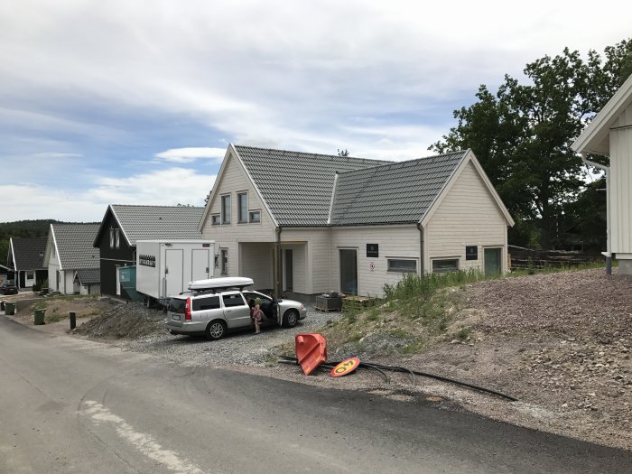 Nybyggda hus med grus och en parkerad bil, indikerar pågående byggarbete och markarbete.