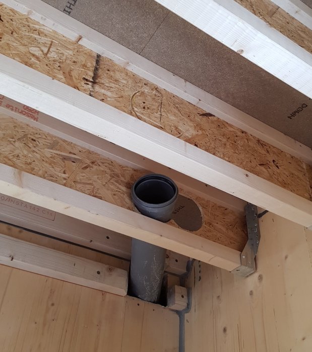 Ventilationströr installerade mellan träbjälkar i taket under konstruktion.