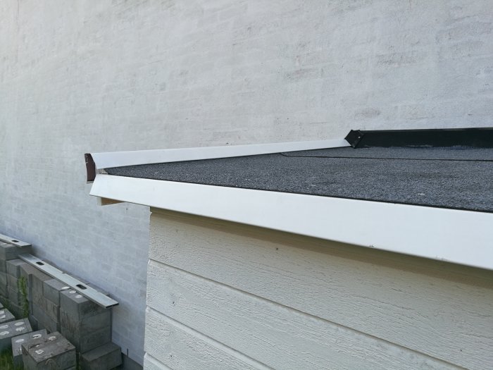 Nybyggt plant tak med tätskikt och vitmålad takfot nära en vit vägg.