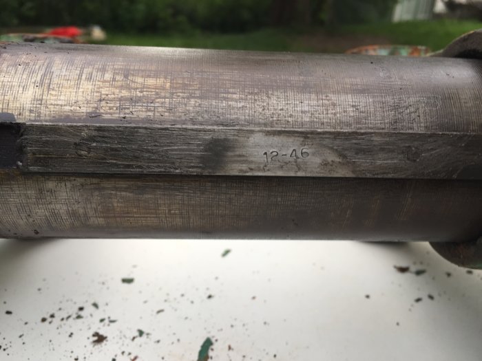 Närbild av en metallstång på ett skruvstäd med stämpeln "12-46", vilket visar tillverkningsdatumet, rengjord med slipmärken synliga.