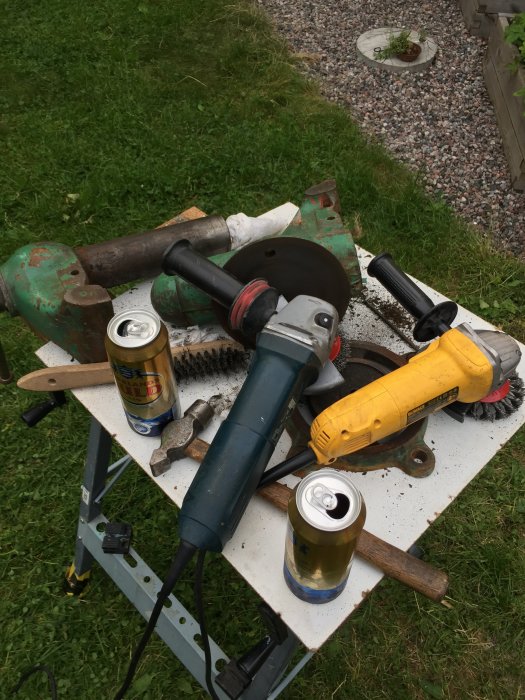 Restaureringsprojekt av gammalt skruvstäd med verktyg, stålborstar och dryckesburkar på arbetsbänk.