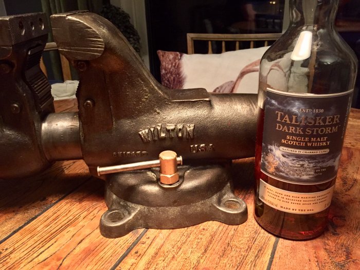 Restaurerat gammalt Wilton skruvstäd från 1941 bredvid en flaska Talisker whisky på ett träbord.