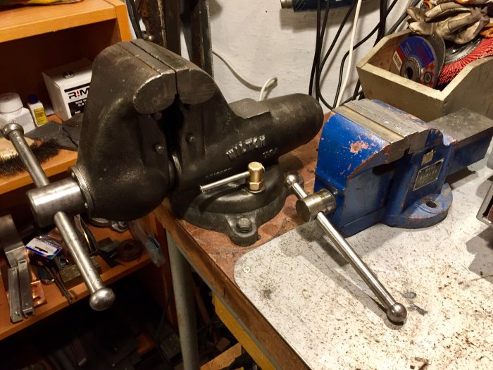 Ny Wilton skruvstycke bredvid ett äldre blått Mount Tai Brand Bench Vice på en verkstadsbänk.