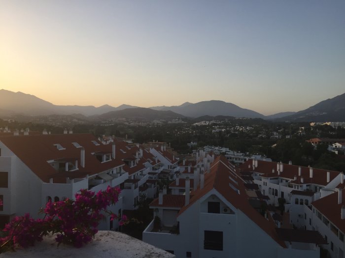 Vy över vita byggnader med röda tak i förgrunden och berg i skymningen i bakgrunden i Puerto Banus.