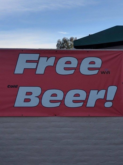 Rosa skylt med texten "Free Beer!" och "Cold" i mindre bokstäver ovanpå, samt WiFi-symbol i övre högra hörnet.