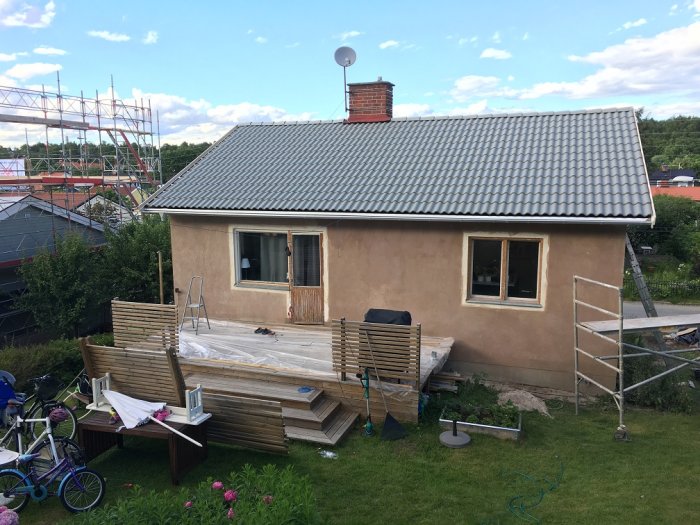 Hus under renovering med grundmålad fasad och påbörjad målning av takfot, byggmaterial framför.