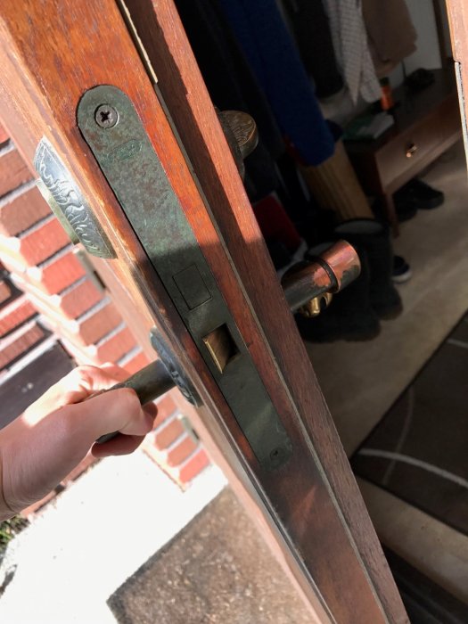 Hand håller nyckel i låscylinder på äldre träentrédörr med synlig låsmekanism.