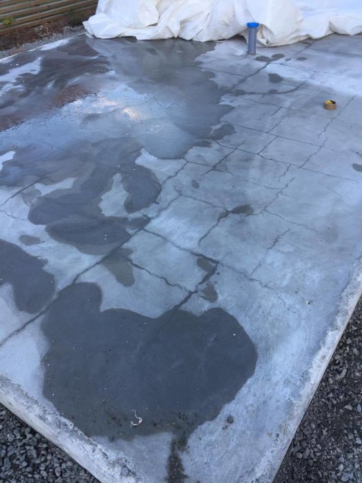 En våt betongplatta med många synliga sprickor och ojämn yta, indikerar potentiella skador på ytan.