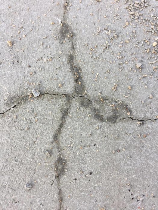 Sprickor i en grå betongplatta med små gruspartiklar på ytan.