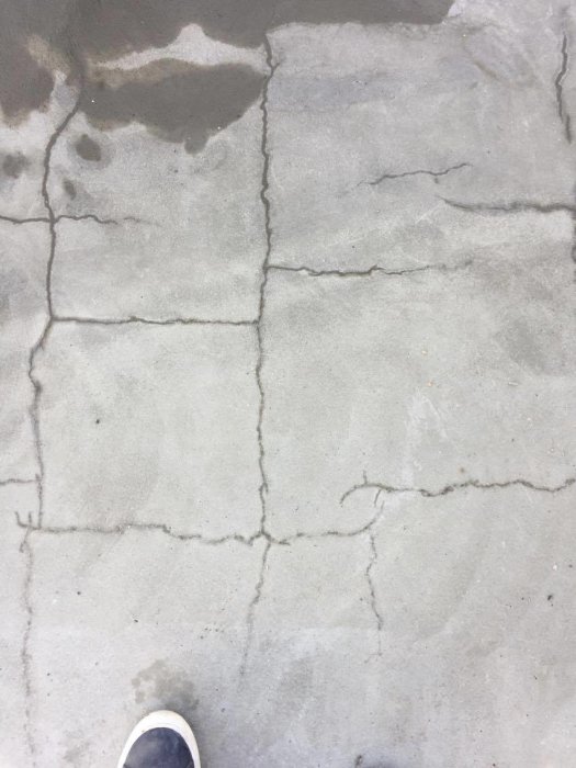Grå betongplatta med flertalet sprickor och fuktfläckar, bildadels synlig skosula nederst.