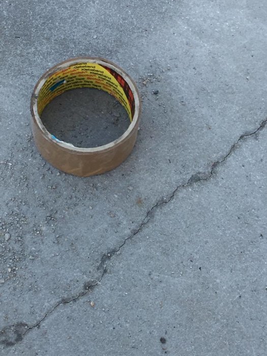 En tejp-rulle ligger nära en spricka på en grå betongplatta som ser nylagd ut.