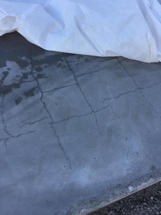 En betongplatta med flera synliga sprickor, delvis täckt av en vit presenning.