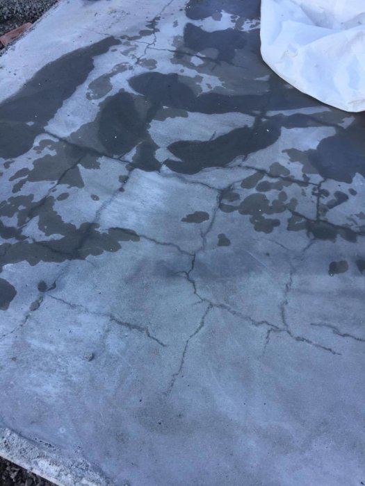 Betongplatta med flera synliga sprickor och vattenfläckar på ytan.