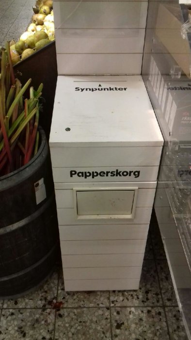 Vit låda för synpunkter ovanpå en papperskorg i en matbutik, ironisk kontext för återkoppling.