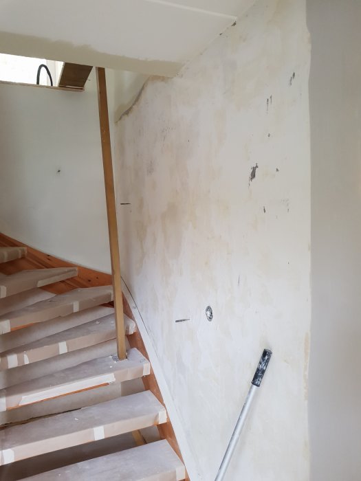 Skrapad vägg vid trappa med synliga spackelspår och renoveringsverktyg.
