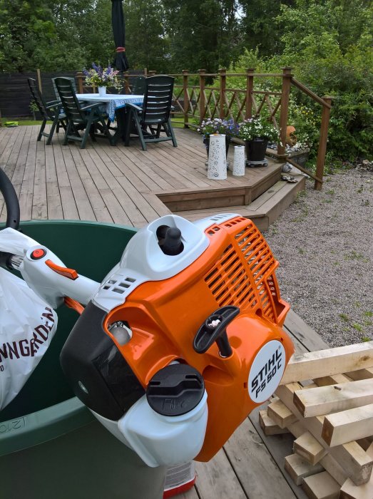 Orange och vit lövblås från Stihl på en altan med träbord, stolar och grönskande omgivning.