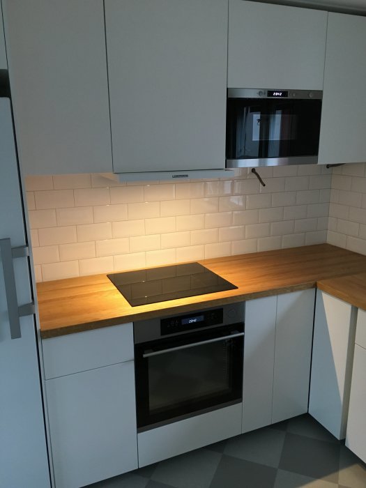 Nytt modernt kök med installerad ugn, mikrovågsugn och induktionshäll på bänkskiva av trä.