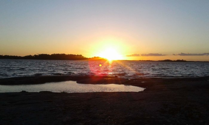 Solnedgång över vattnet i S:t Anna skärgård med siluetter av träd och klippor.