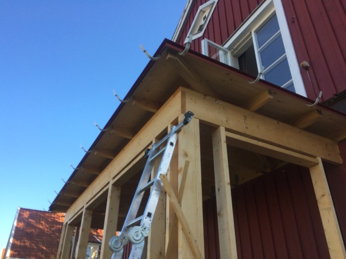 Installation av rännkrokar på en träkonstruktion vid ett rött hus med stegar lutade mot fasaden.