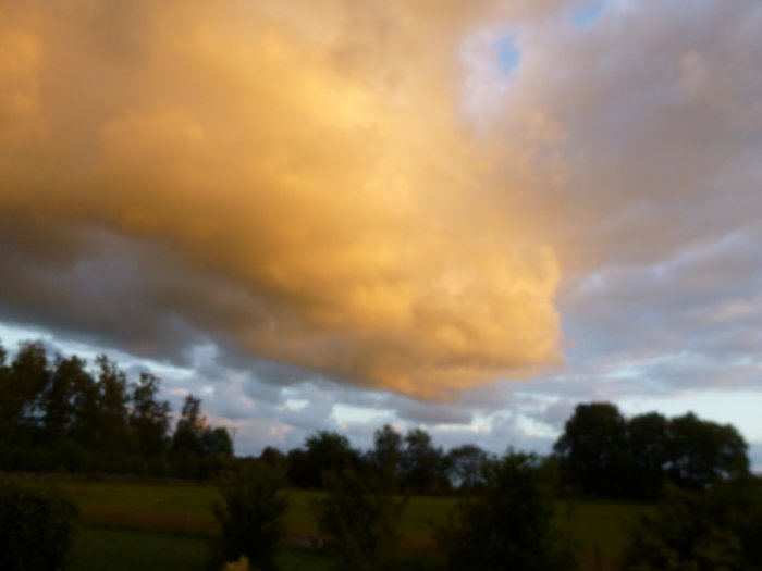 Kvällshimmel med stora moln belysta underifrån ovanför ett lantligt landskap.