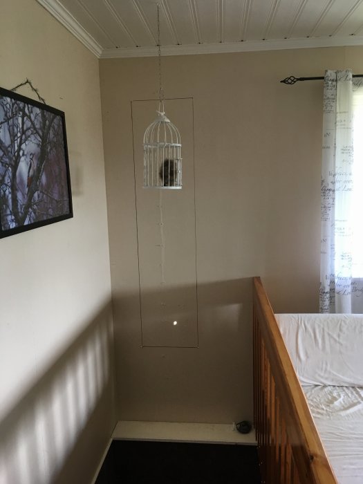 Ett fönster som är placerat åt sidan ovanför en trappa, med en fågelbur hängande framför och gardiner till höger.