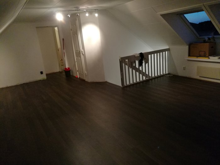 Renoverat övre plan med mörkt laminatgolv, nyinstallerade vita dörrar och räcke vid trappan.