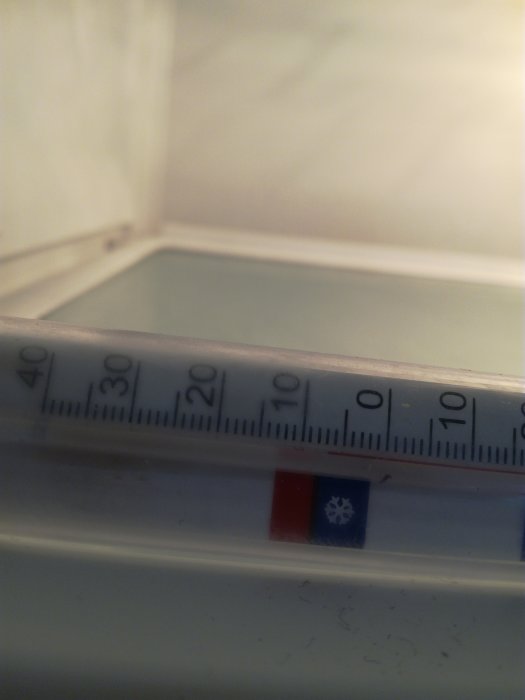 Termometer inuti ett kylskåp som visar cirka två grader Celsius, suddig bakgrund av kylens inre.