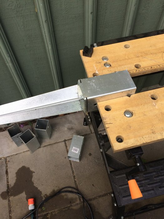 En arbetsbänk med en fastklämd metallprofil och flera metallklossar på marken bredvid.