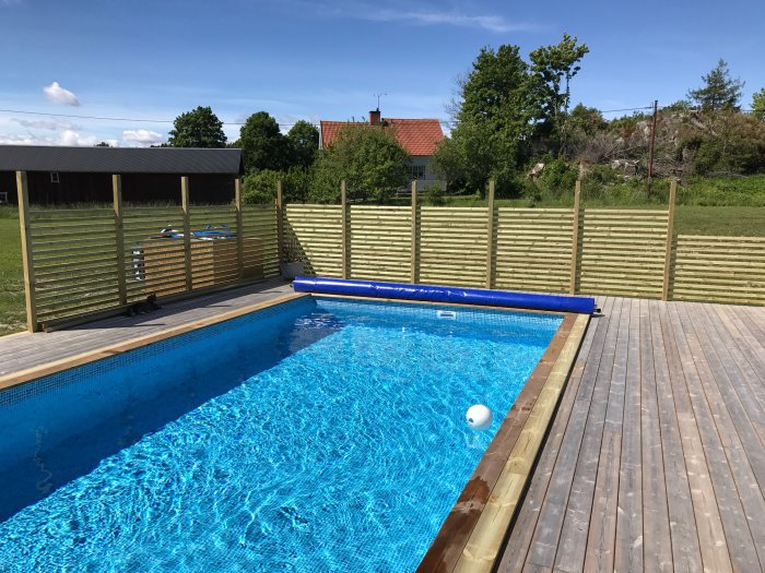 Utomhuspool med nybyggt trädeck och påbörjat räcke under en klarblå himmel.