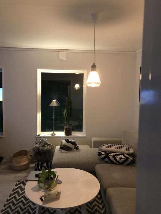 Vardagsrum med lampa som inte är centrerad över det vita soffbordet, bredvid en soffa och ett fönster.