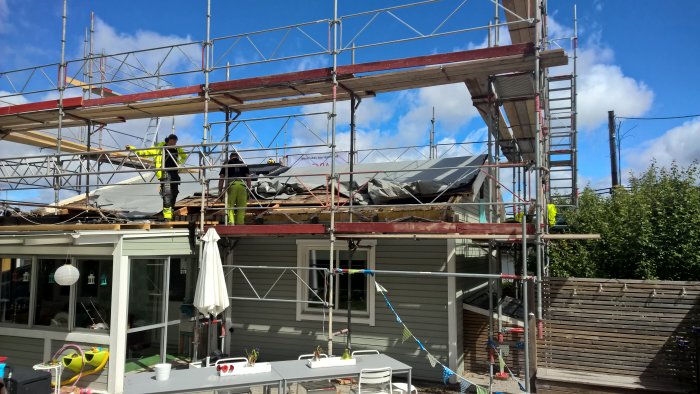 Arbetare på byggnadsställning tar bort takstolsspetsar från ett hus.