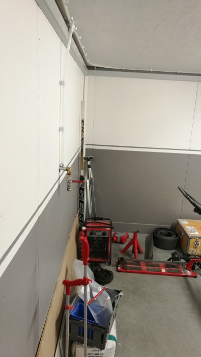 Tryckluftsinstallation med rör och uttag på väggen i ett garage fullt av verktyg och utrustning.