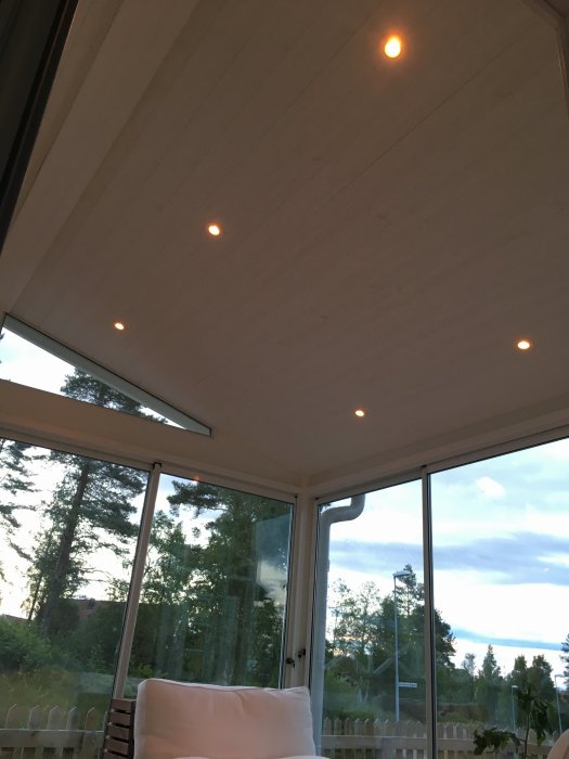 Uterum med tända spotlights i taket, dubbeluttag och stora fönster mot skog.