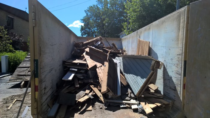 Nedrivet tak och takstolar i en container under en solig himmel, arbetsrenovering pågår.