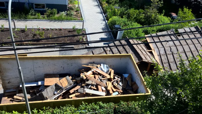 Vy från ovan av en byggarbetsplats med en container full av rivningsavfall och en omgivande trädgård.