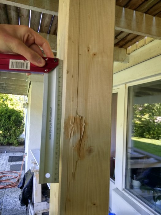 Nyinstallerad limträbalk med en synlig stor spricka mäts med en vinkelhake utomhus nära tak och balkong.