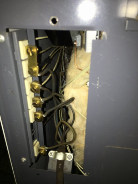 Öppen säkringsskåpspanel som visar gammal elektrisk inkoppling med kablar och säkringsfästen.