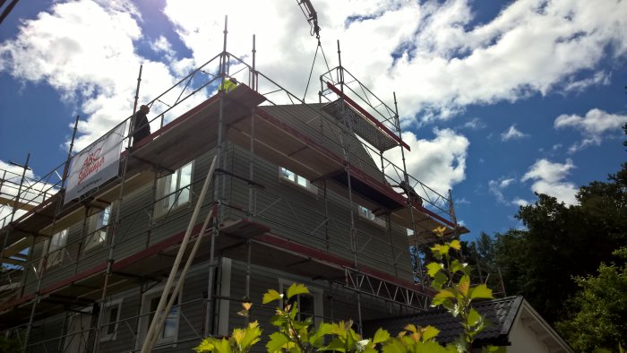 Hus under renovering med nytt bjälklag och väggkonstruktioner, omgiven av byggnadsställningar och en klarblå himmel.