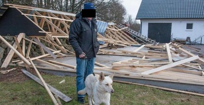 Person och hund framför en hoprasad träkonstruktion efter stormen Gorm.