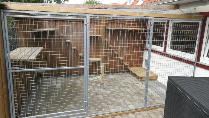Kattgård med metallsektioner, nät och klätterhyllor vid ett radhus, utan katter synliga.