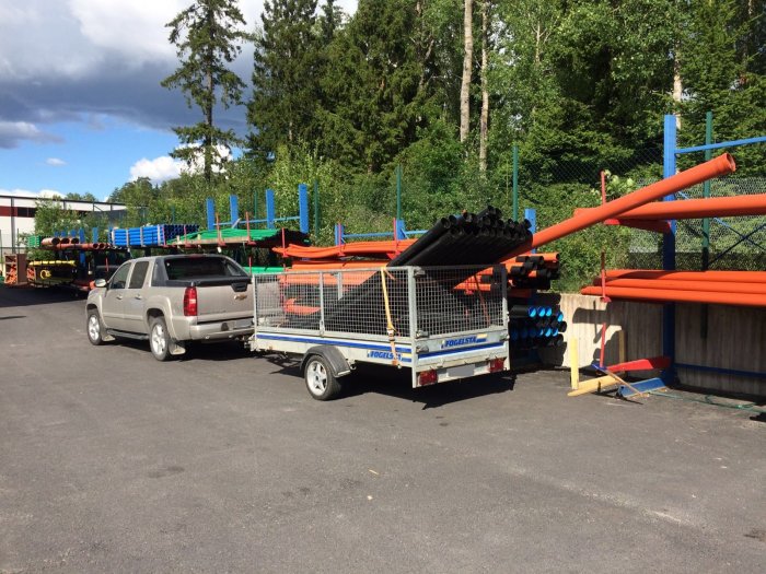 SUV kopplad till en Thule släpvagn lastad med orange och svarta plaströr på en industriplats.